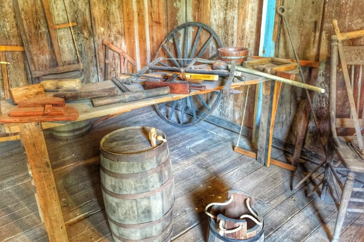Rustic workshop with wooden tools, barrels, and a wagon wheel in a wooden-walled room.