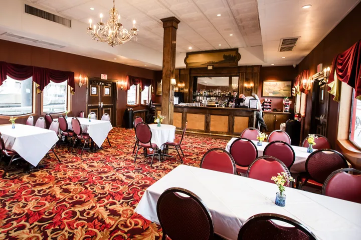 Elegant restaurant interior with red chairs, white tablecloths, floral carpet, and chandelier.