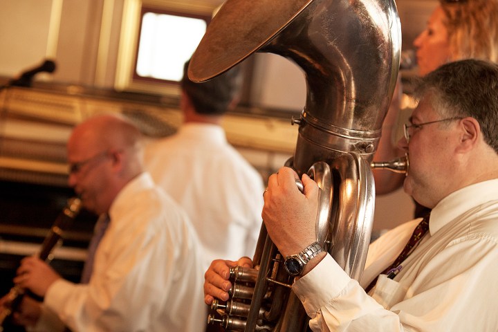 Musicians playing a clarinet and a sousaphone in a warm-lit room.