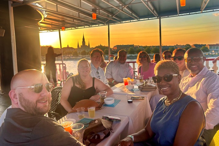 Group of people smiling at a table on a boat during sunset.