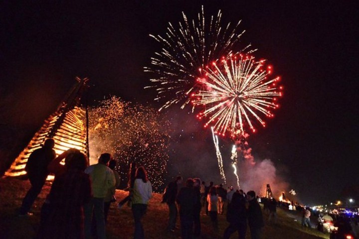 People watch fireworks and a bonfire at night.