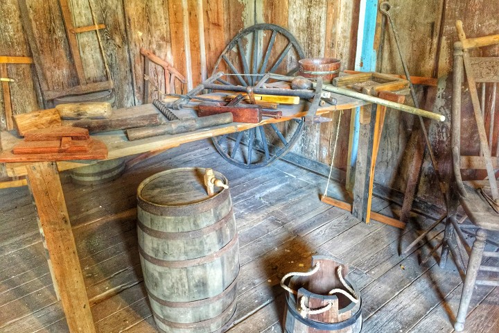 Rustic workshop with wooden barrel, wagon wheel, tools, and wooden walls.