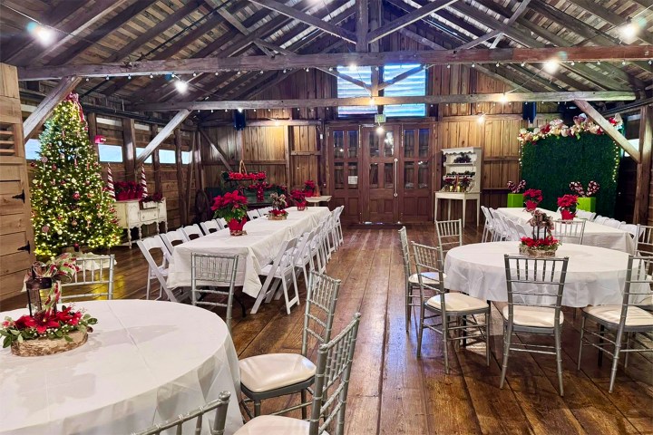 Rustic hall with Christmas decorations, round tables, white chairs, and a Christmas tree.