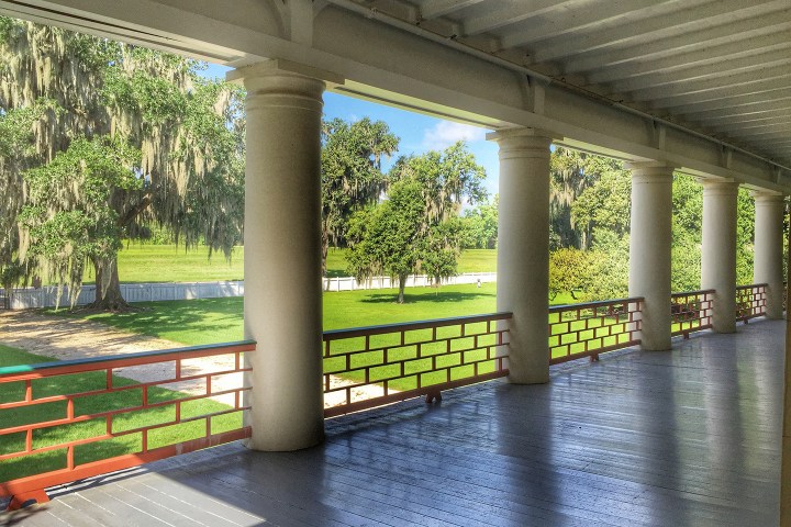 Veranda with columns overlooking a scenic, grassy landscape with trees and a fence.
