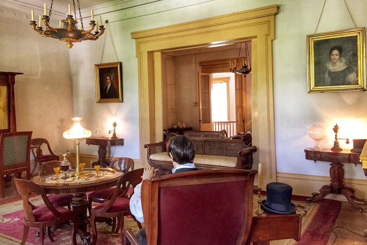 Vintage room with portraits, chandelier, furniture, and man seated.