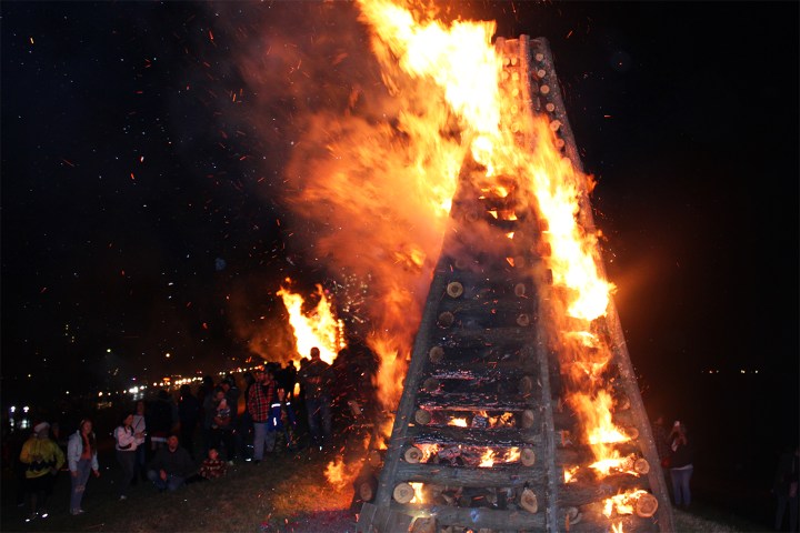Large bonfire with people gathered around at night.
