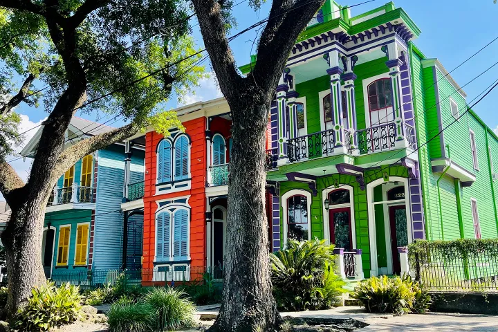 Colorful historic houses in blue, red, and green, with large trees in foreground.