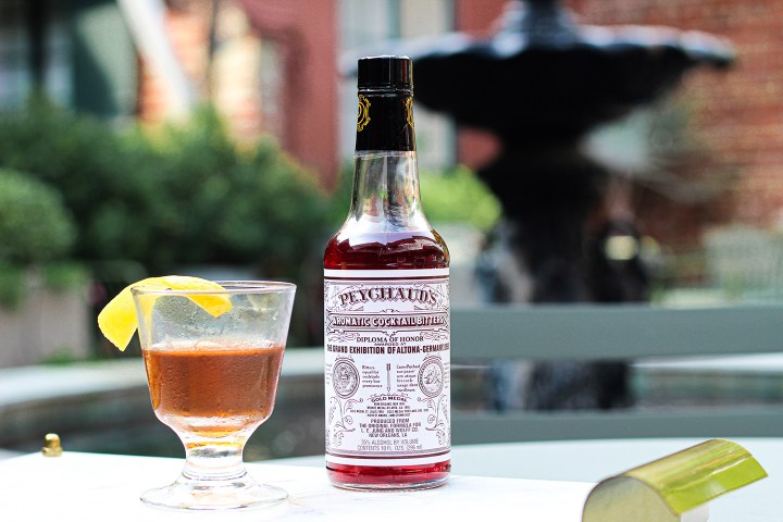 A bottle and glass of Peychaud's Bitters on a table outdoors.