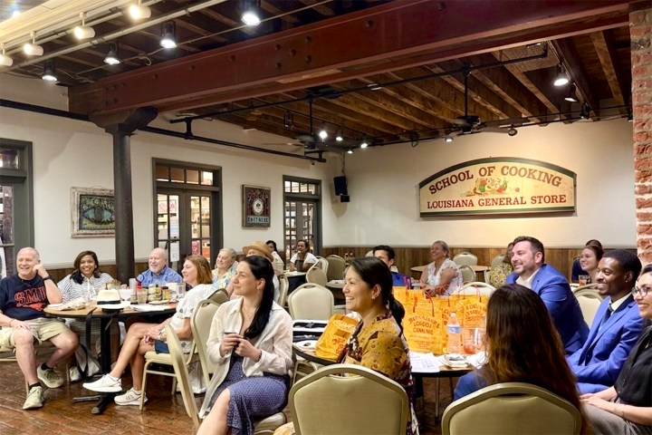 People seated in a room with a School of Cooking sign, engaged in a presentation.