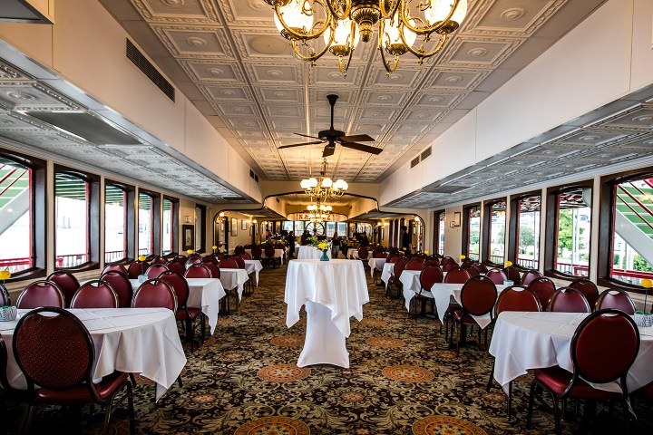 Elegant dining room with chandeliers, tables with white cloths, and large windows.