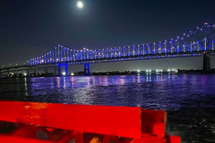 Bridge illuminated with blue lights over a river at night; moon visible in the sky.