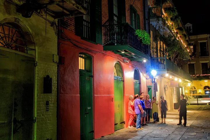 Group of people stand outside a colorful street building at night.