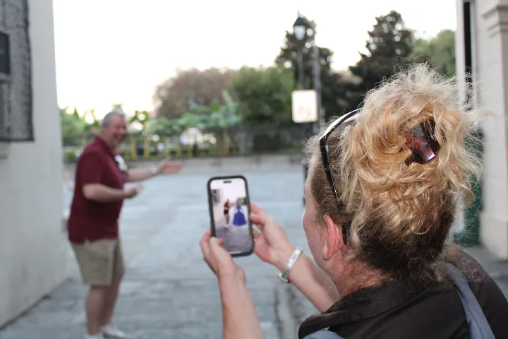 Woman taking a photo with a phone of a man posing on a street.