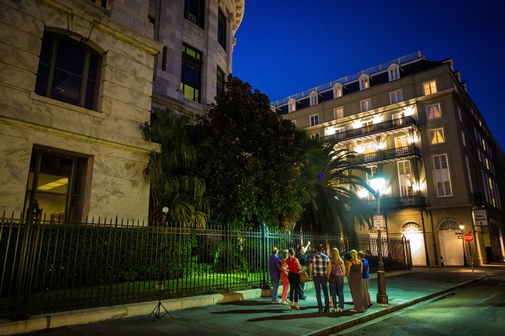Group of people gathered near lit historic buildings and palm trees at night.