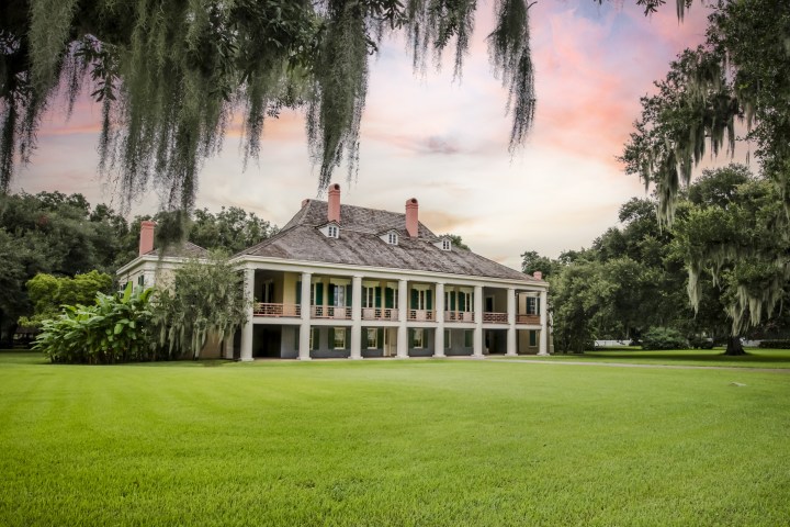 a large green field with trees in the background with Destrehan Plantation in the background