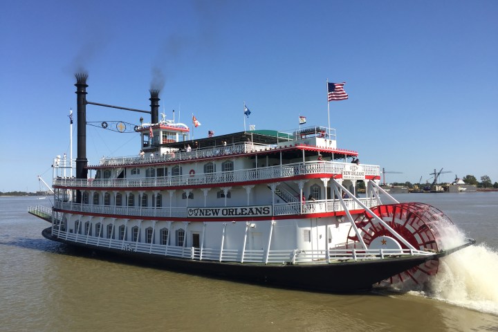 Paddle steamboat 'City of New Orleans' on a river with blue sky background.