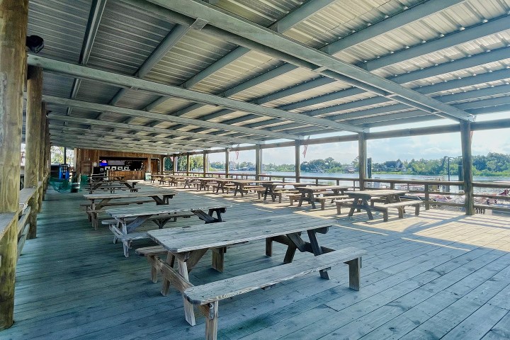 Covered outdoor seating area with wooden picnic tables overlooking a river.