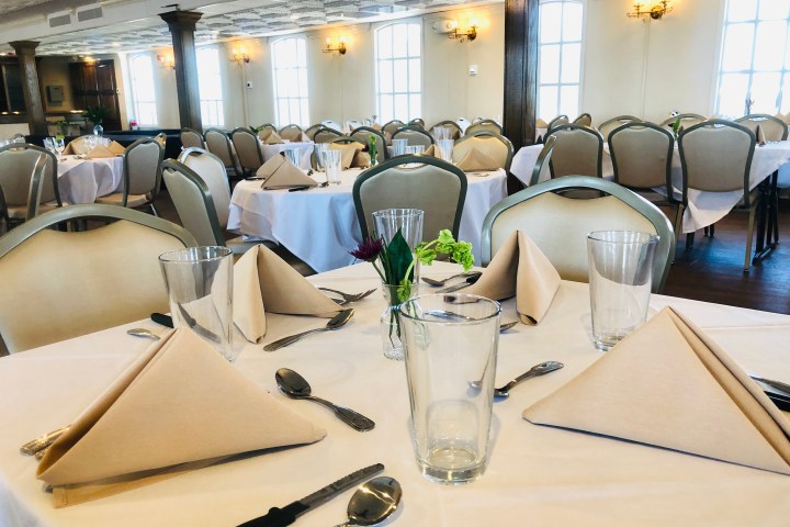 Elegant dining room with neatly set tables, folded napkins, and glassware.