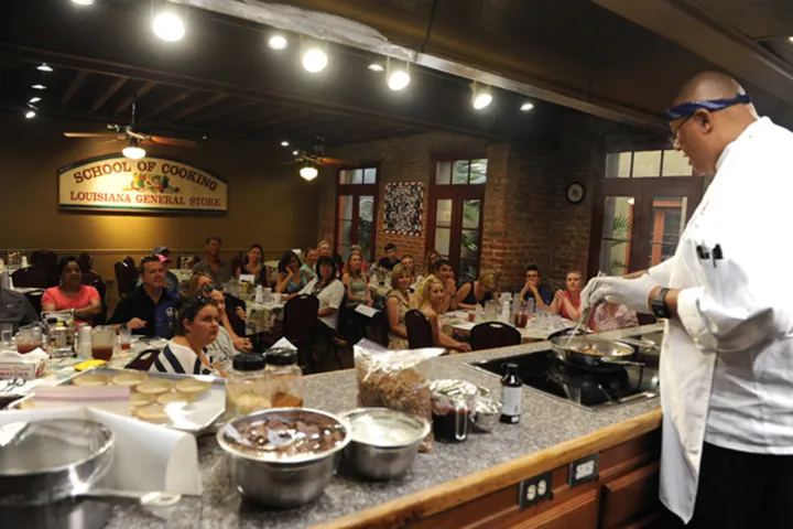 Chef conducting a cooking class in front of seated audience at a Louisiana culinary school.