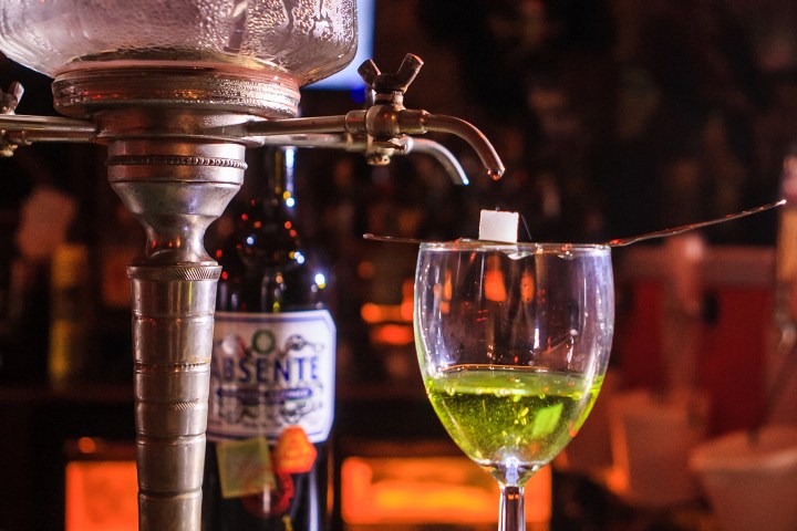 Absinthe fountain with glass, sugar cube, and bottle in dim bar setting.