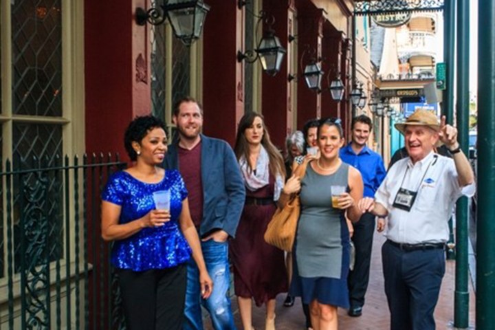 Group of people walking on a city street, some holding drinks, with a guide gesturing.
