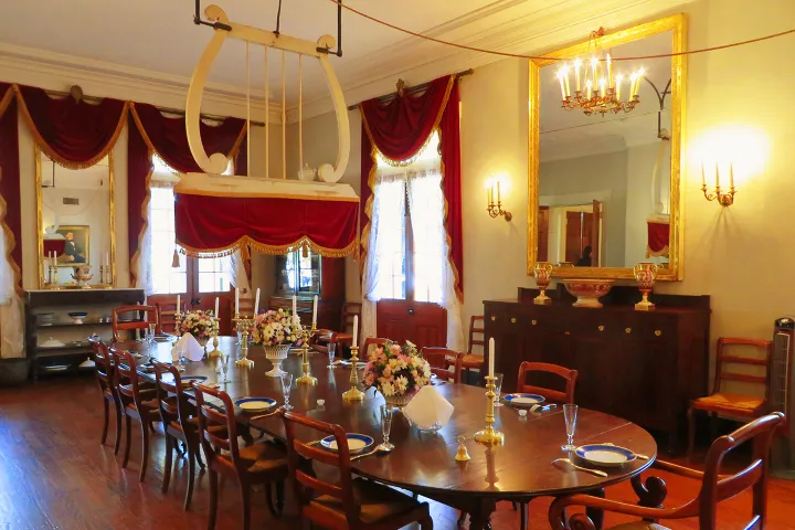 Elegant dining room with a large wooden table, red curtains, mirror, and chandelier.