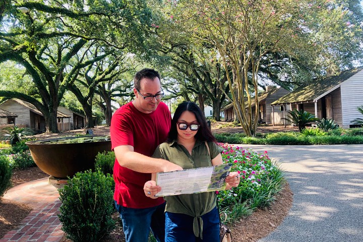 Two people reading a map in a garden with historic wooden buildings in the background.