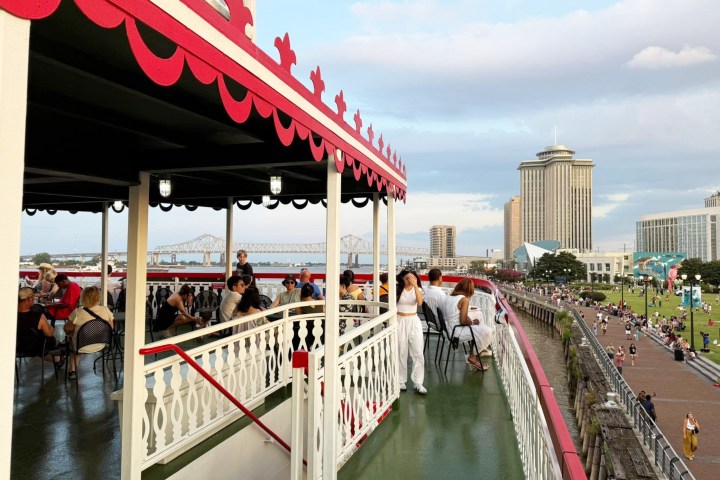 People on a riverboat deck by a city skyline with a bridge in the background.