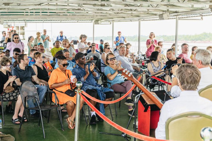 People seated on a boat, watching and clapping at a live music performance.
