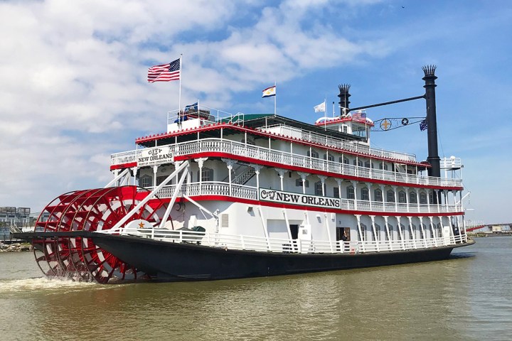 Paddle steamboat on water with red wheel and flags.