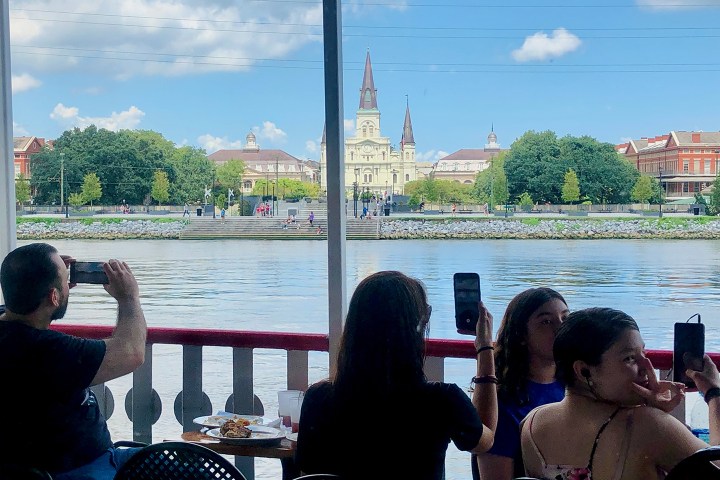 People taking photos on a boat with a view of a historic building across the water.