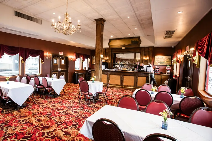 Elegant restaurant interior with chandeliers, red carpet, tables with white cloths, and a wooden bar.