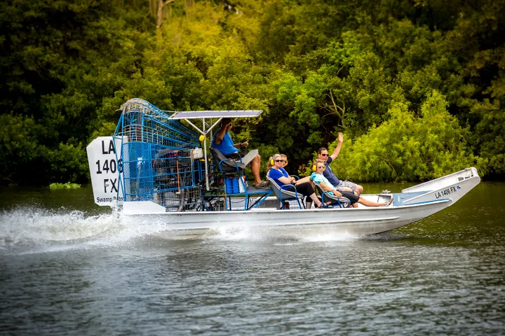 Airboat with five people cruising on a river surrounded by dense greenery.