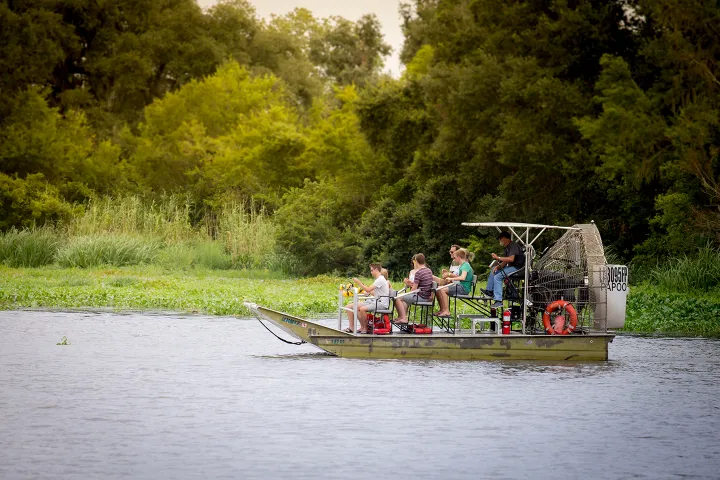 Group of people on an airboat touring a green river landscape with dense trees.