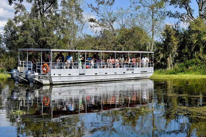 Tour boat on a lake with passengers, surrounded by trees and reflecting water.