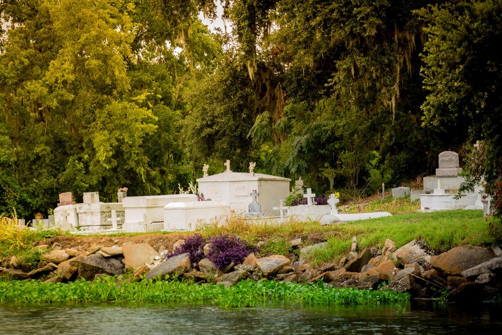 Above-ground graves surrounded by trees near a water's edge in a cemetery setting.