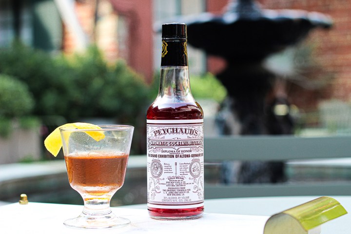 Cocktail glass with lemon twist and bitters bottle on outdoor table.
