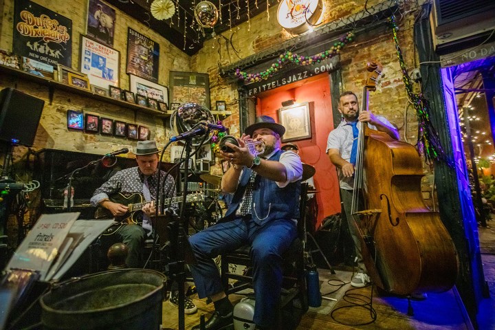 Jazz band performs with trumpet, guitar, and double bass in a cozy, decorated room.