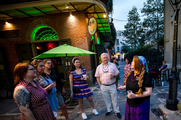 Group of people in costumes standing outside a building with green lights and an umbrella.