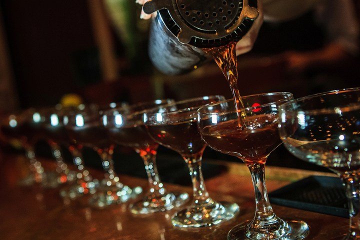 Bartender pouring cocktails into glasses on a bar counter.