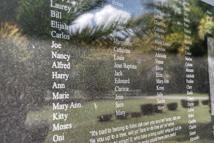 Names etched on a reflective memorial wall with garden in the background.