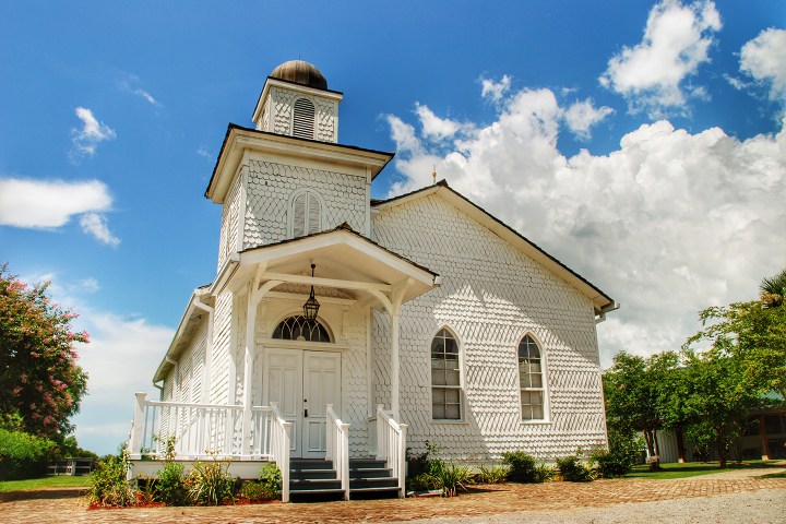 White historic church with steeple under a blue sky with clouds.