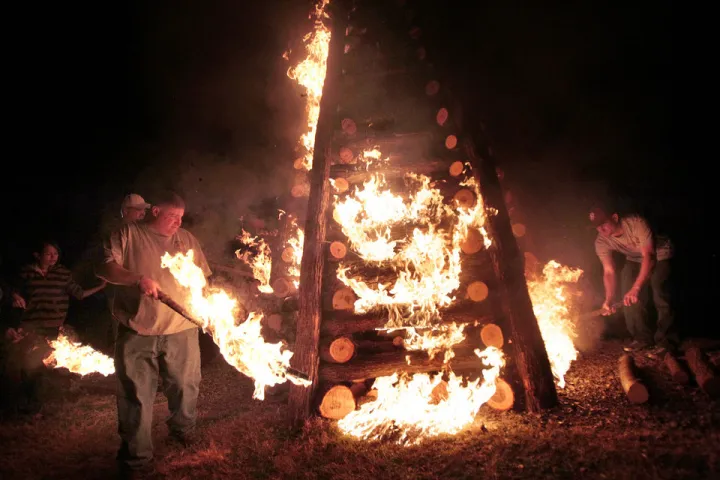People lighting a large wooden pyramid structure on fire at night.