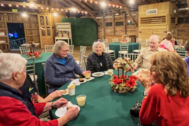 Group of people sitting around a festive table with holiday decorations in a wooden hall.