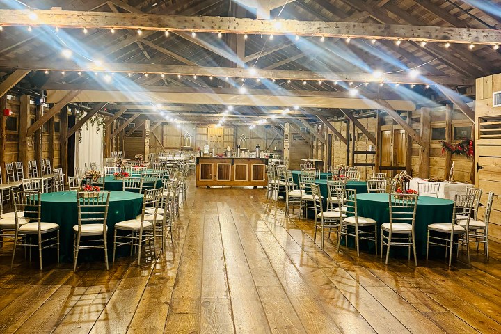 Rustic event hall with round tables, green tablecloths, and string lights.