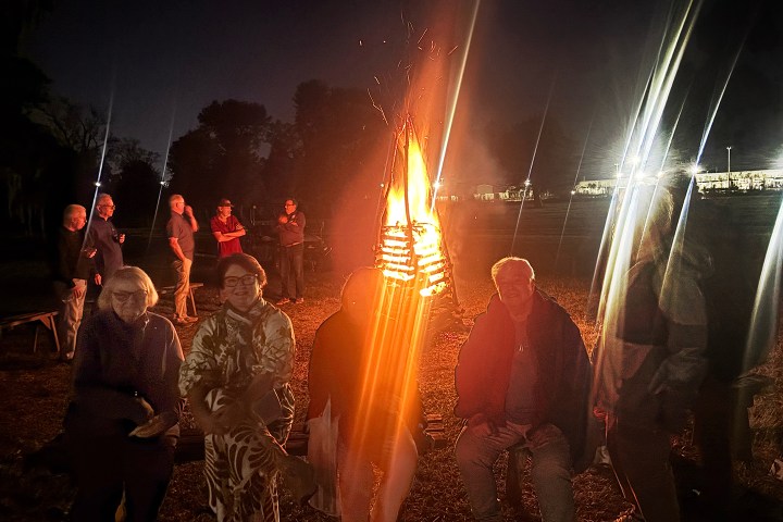 Group of people sitting and standing around a bonfire at night.