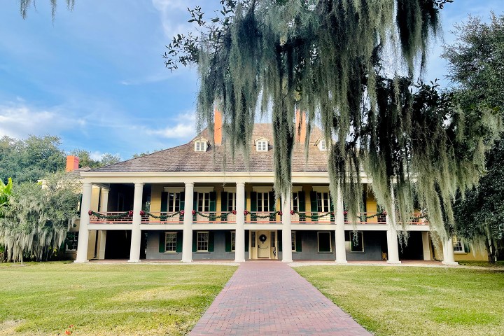 Historic two-story house with columns and Spanish moss, fronted by a brick walkway.