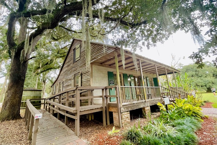 Historic wooden house with porch, surrounded by trees and greenery.