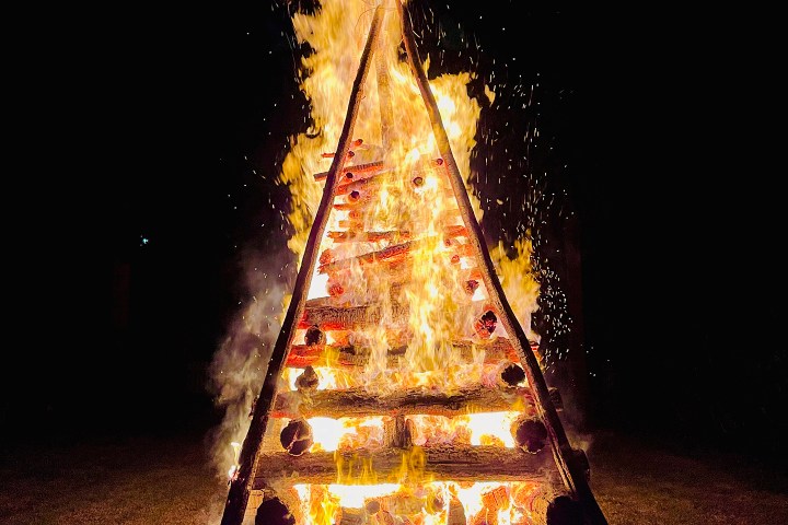 Triangular log stack on fire blazing brightly against a dark background.