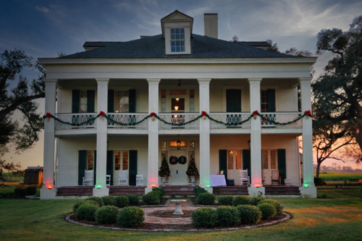 White colonial house with columns, Christmas decorations, and a garden in front.